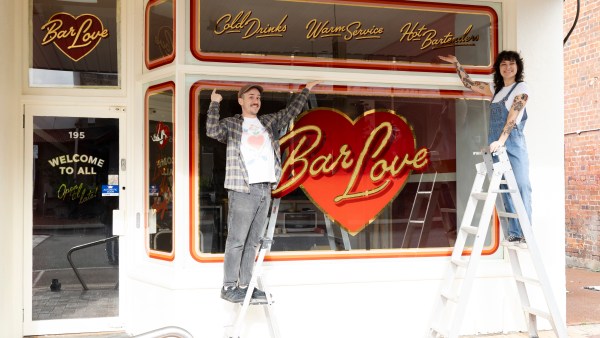 Pippa Canavan and Murray Walsh stand on ladders out the front of Bar Love. On the window, Bar Love is written in gold.