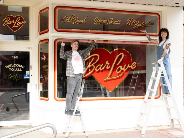 Pippa Canavan and Murray Walsh stand on ladders out the front of Bar Love. On the window, Bar Love is written in gold.