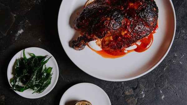 Harissa chicken and sides on white plates, sitting on a black countertop.