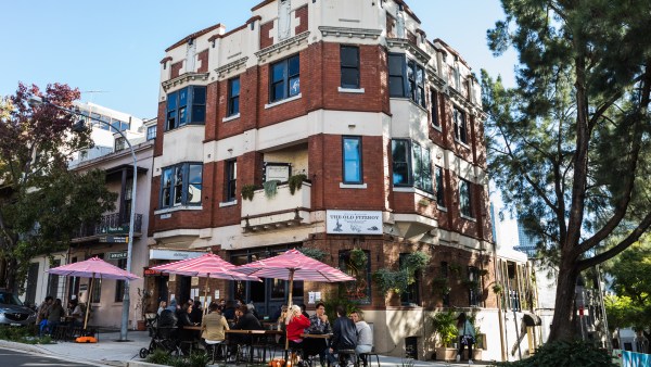 Exterior view of The Old Fitz Woolloomooloo with people sitting on the footpath under red and white umbrellas.