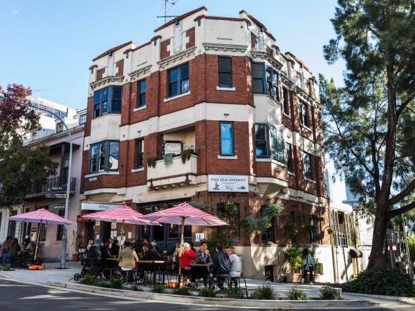 Exterior view of The Old Fitz Woolloomooloo with people sitting on the footpath under red and white umbrellas.