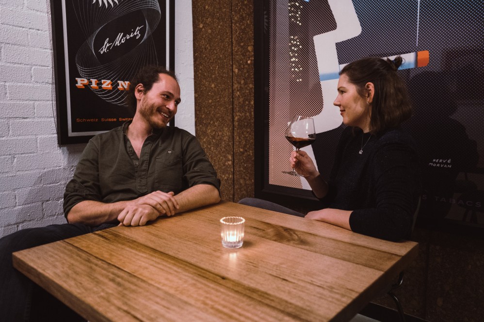 The Art Syndicate co-founders Saxon Strauss and Lisa Guenther-Straus sit together at a bar table drinking wine.