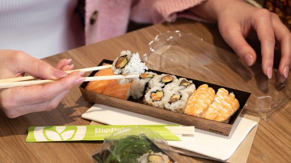 A woman uses wooden chopsticks to eat sushi from a BioPak sushi tray.