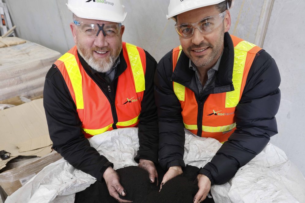 Two men in high vis vests hold bio char coffee in their hands.