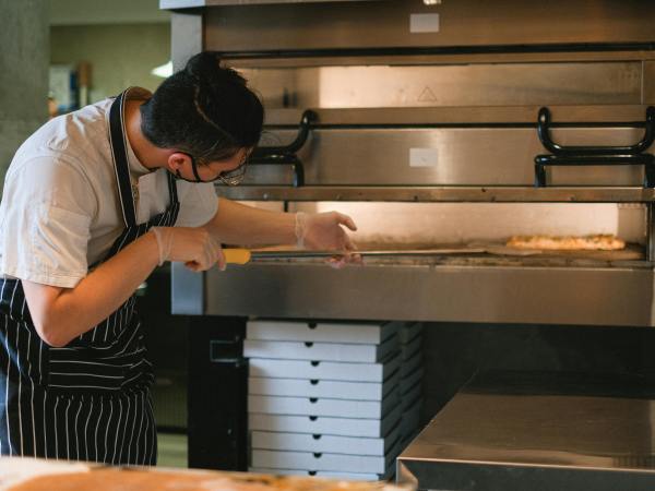 A hospitality worker puts pizza into an oven.