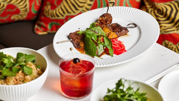 Plates of food at Lúc Lắc in front of a red-cushioned bench seat.