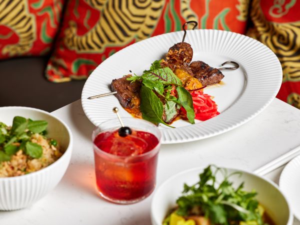 Plates of food at Lúc Lắc in front of a red-cushioned bench seat.