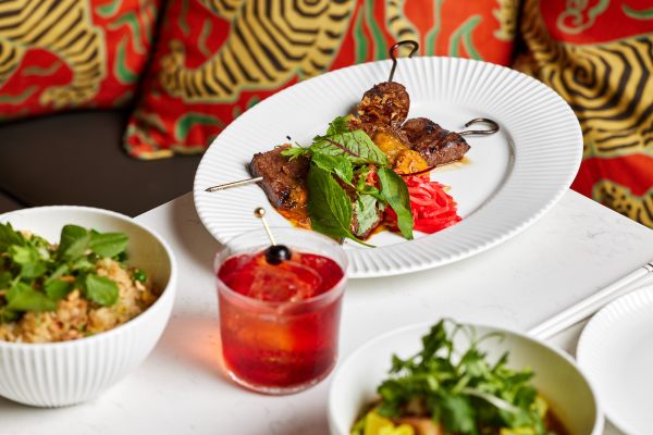 Plates of food at Lúc Lắc in front of a red-cushioned bench seat.