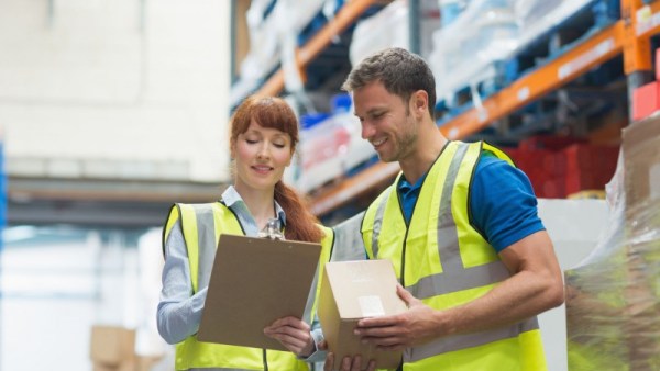 Workers in safety vests checking off a list in a warehouse.