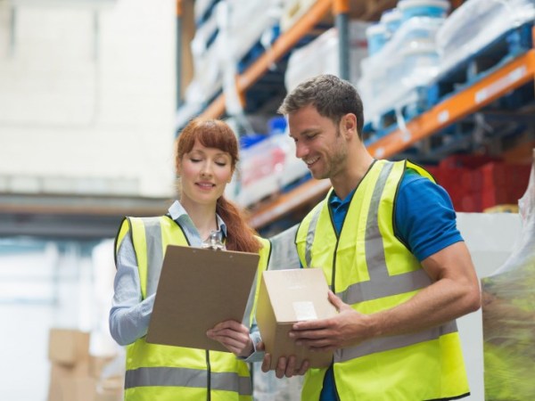 Workers in safety vests checking off a list in a warehouse.