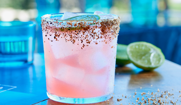 Pale pink margarita in an old fashioned glass with chilli and salt rim against a blue background