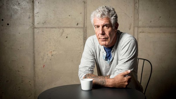 Anthony Bourdain looking at camera, arms folded, leaning on table