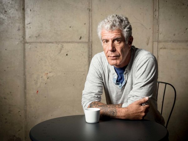 Anthony Bourdain looking at camera, arms folded, leaning on table