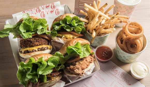 Four burgers from Betty's Burgers, with chips, onion rings and sauce.