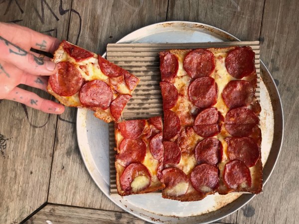 Mary's Detroit style pizza. A square pizza with pepperoni. A hand is pulling a slice away from the plate.